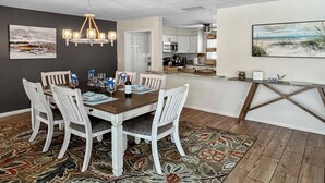 A dining area with a wooden table and white chairs, a chandelier, and a patterned rug. - Coral Sunshine - large south terrace with pool/spa (Cape Coral)