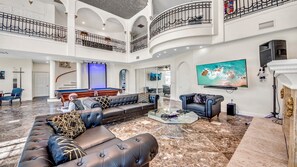A spacious living area with a pool table, leather sofas, a flat-screen TV, and a marble floor.
