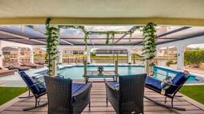 A covered outdoor area with a pool, lounge chairs, and a table.
