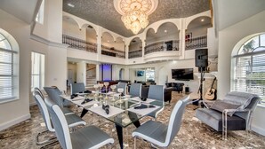 A spacious living area with a glass-top dining table, multiple seating options, a grand chandelier, and a balcony with railings. - Golden Globe - luxury on the canal with pool/spa (Cape Coral)