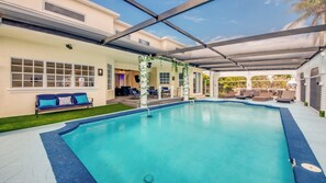 A pool area with a covered patio, seating, and a view of the surrounding landscape.