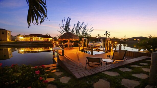A serene outdoor area with a pool, lounge chairs, and a thatched-roof structure, likely for relaxation or dining. - Lupita, boat lift, dock, heated south facing pool (Cape Coral)
