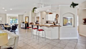 A modern kitchen with a central island, bar stools, and a dining area with a sofa and chairs. - Lupita, boat lift, dock, heated south facing pool (Cape Coral)