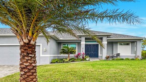 A single-story house with a grey exterior, a dark blue front door, and a small porch with a chair. - Phoenix, quite Area, Pool and great water few (Cape Coral)