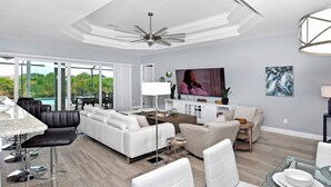 A modern living room with a large TV, seating area, and a view of the outdoors. - Phoenix, quite Area, Pool and great water few (Cape Coral)