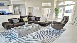 A modern living room with a sectional sofa, a glass coffee table, and a patterned rug. - Rosegarden - Pool/Spa and perfect water view (Cape Coral)