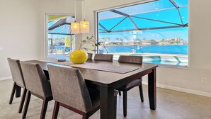 A dining area with a large window overlooking a pool and a view of the sea. - Rosegarden - Pool/Spa and perfect water view (Cape Coral)