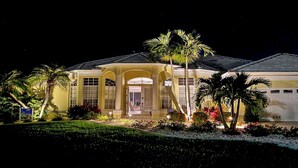 A large, yellow building with a central entrance, surrounded by palm trees and well-maintained gardens. - Rosegarden - Pool/Spa and perfect water view (Cape Coral)