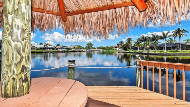 A wooden dock with a thatched roof, a calm water body, and a clear sky. - Rosegarden - Pool/Spa and perfect water view (Cape Coral)