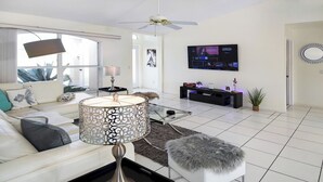 Un salon moderne avec un canapé blanc, un lampadaire à motifs, une table basse en verre et un téléviseur fixé au mur.