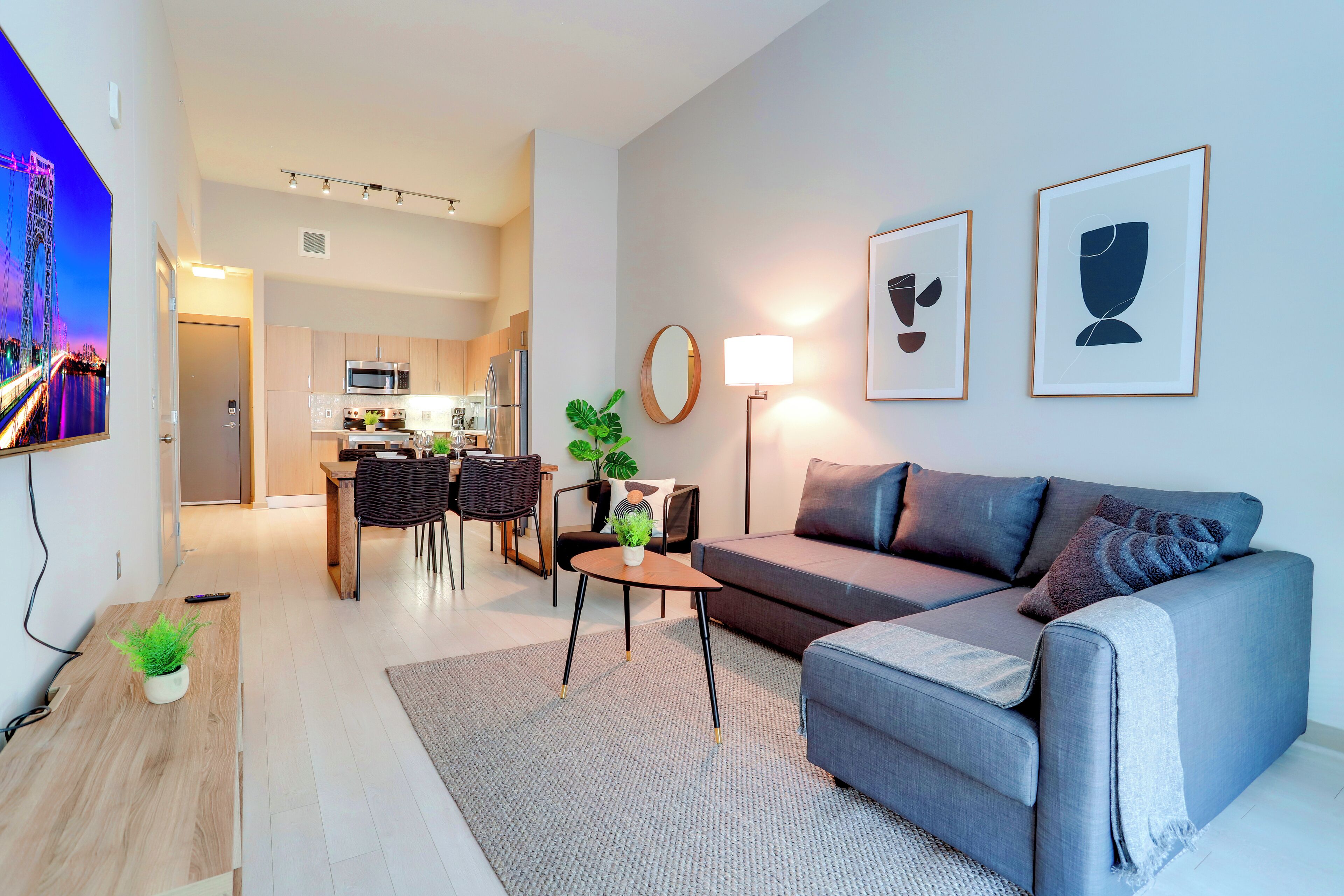 A modern living room with a grey sofa, a dining area with a table and chairs, and a kitchen in the background.