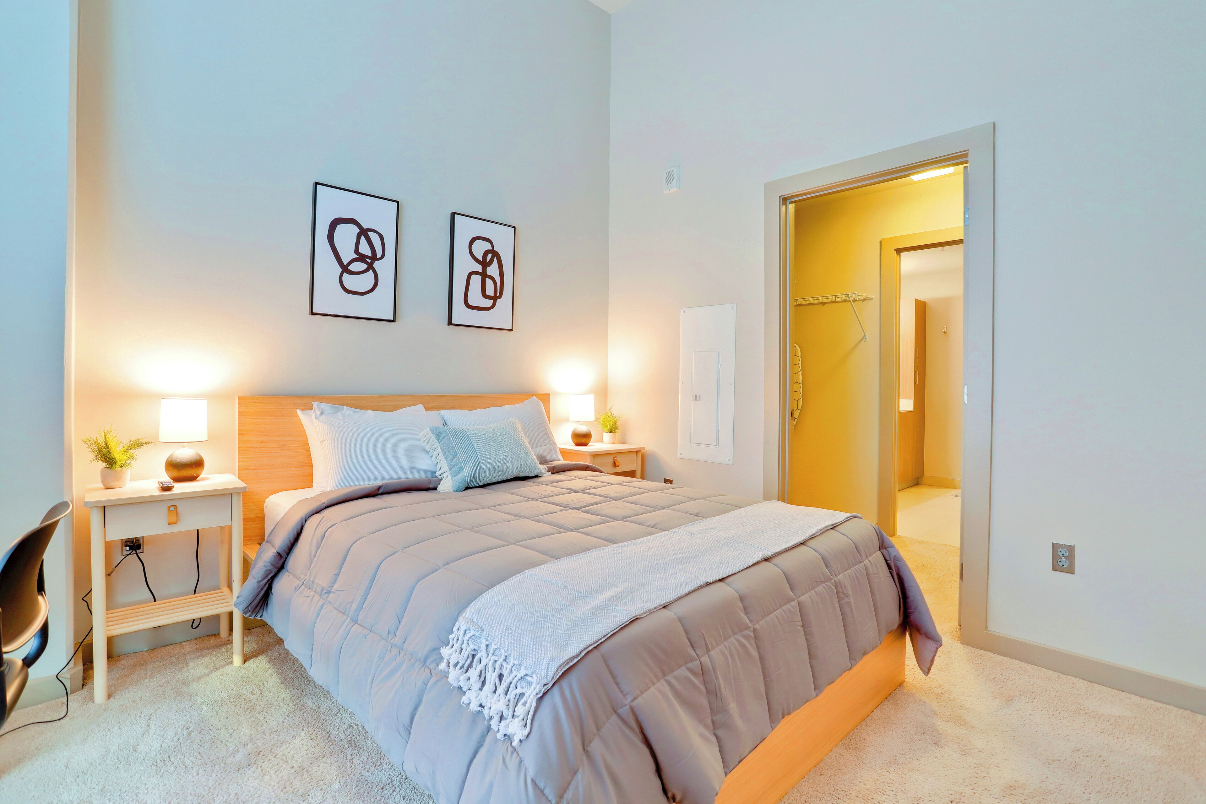Une chambre à coucher moderne avec un grand lit, des tables de chevet, une chaise et des œuvres d’art accrochées au mur.
