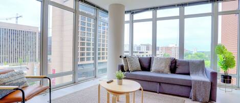 A modern living room with a sofa, a coffee table, and a large window offering a city view.