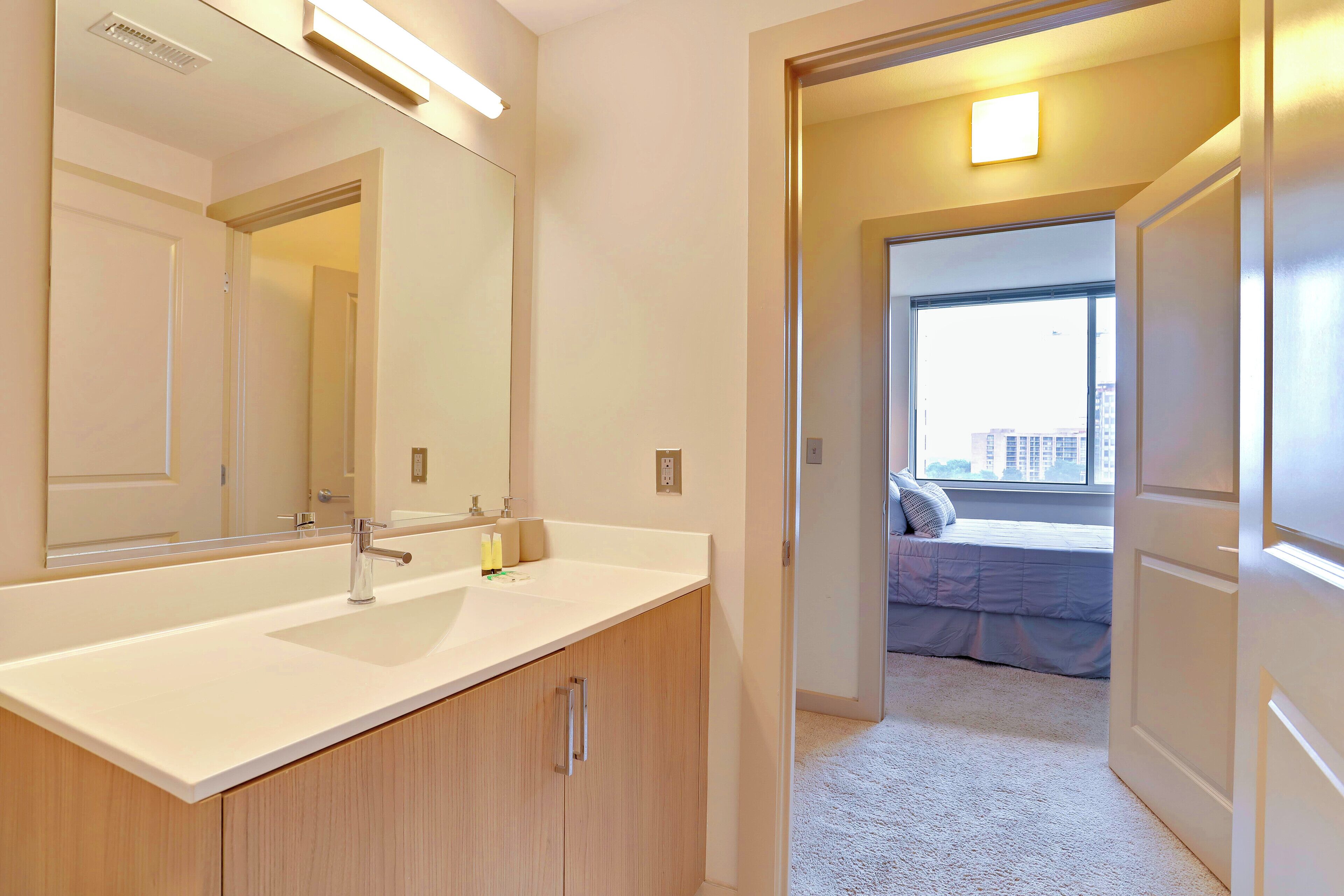 A modern bathroom with a large mirror, a white sink, and wooden cabinets.
