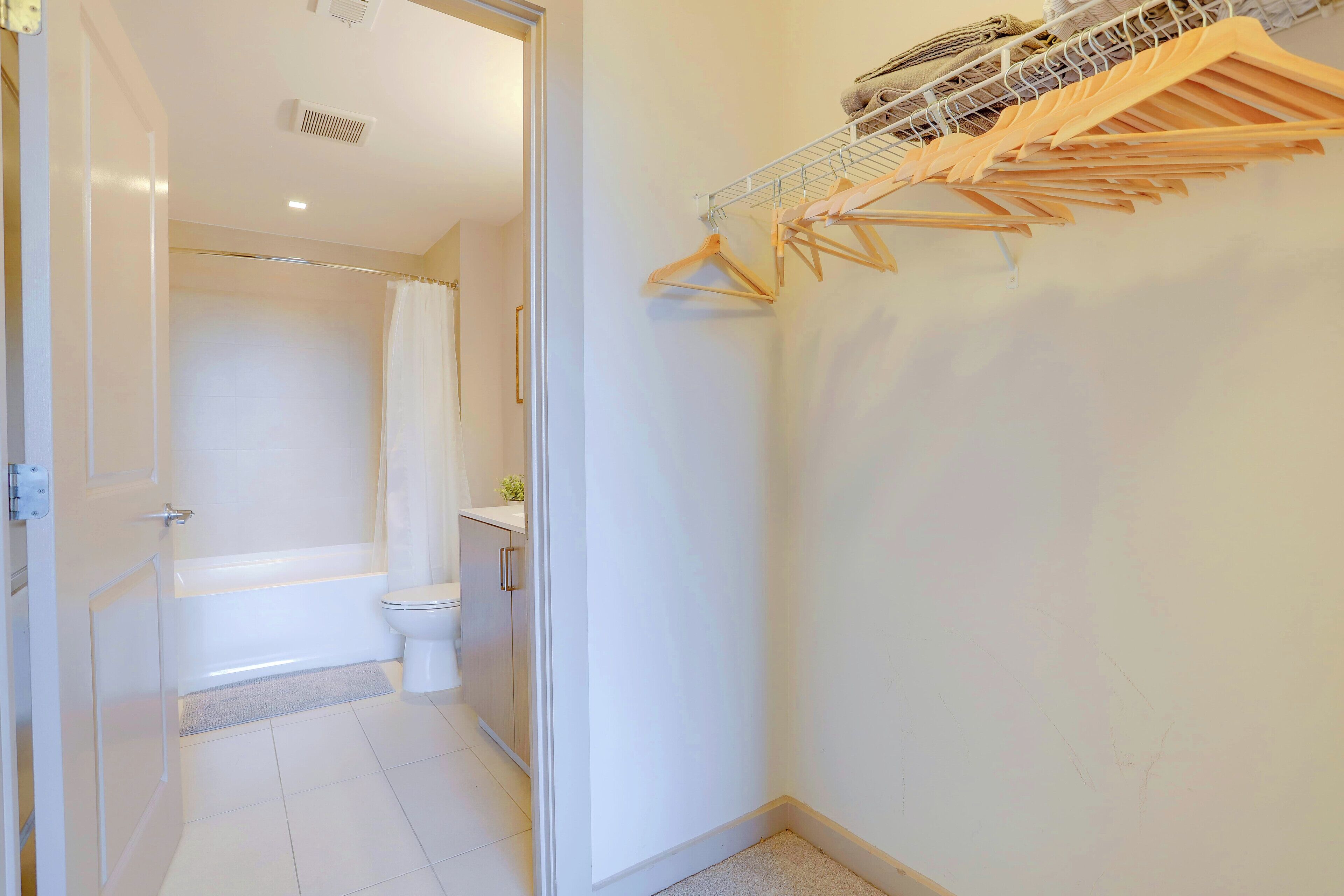A bathroom with a bathtub, toilet, and a shower curtain. There is a wooden drying rack with clothes hanging on it.