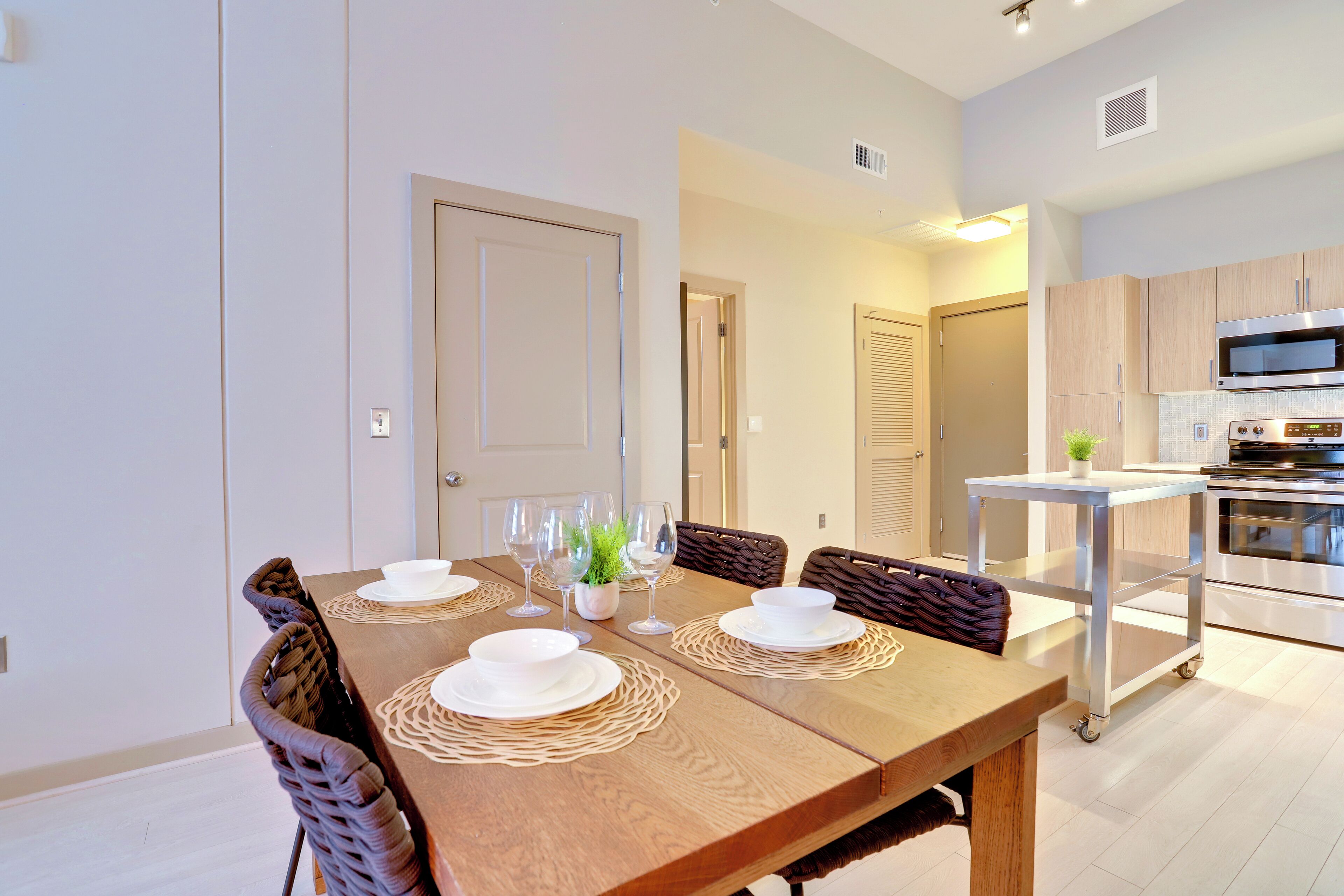 A dining area with a wooden table set for four, surrounded by wicker chairs.