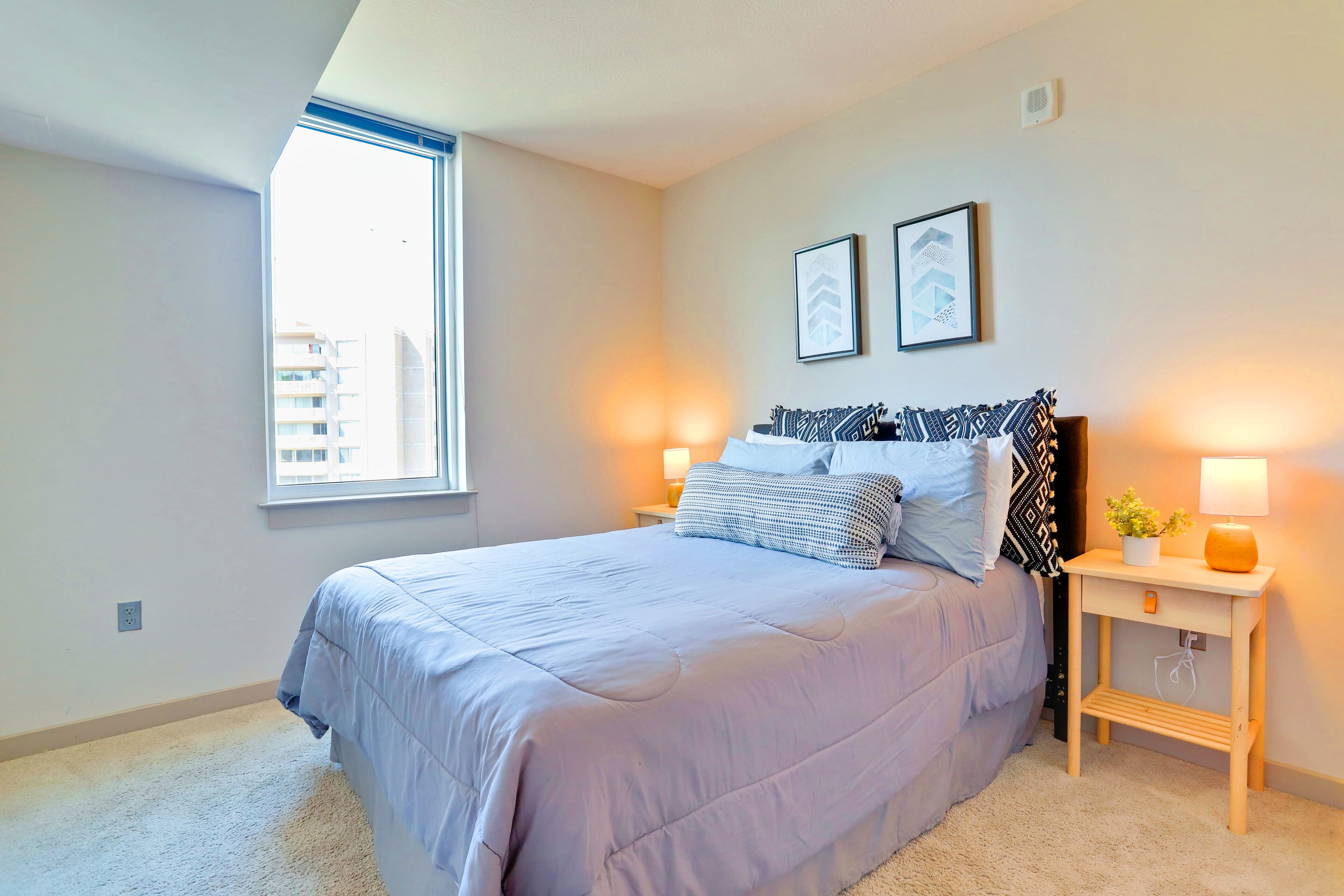 A bedroom with a large bed, two bedside tables, a window, and two framed pictures on the wall.