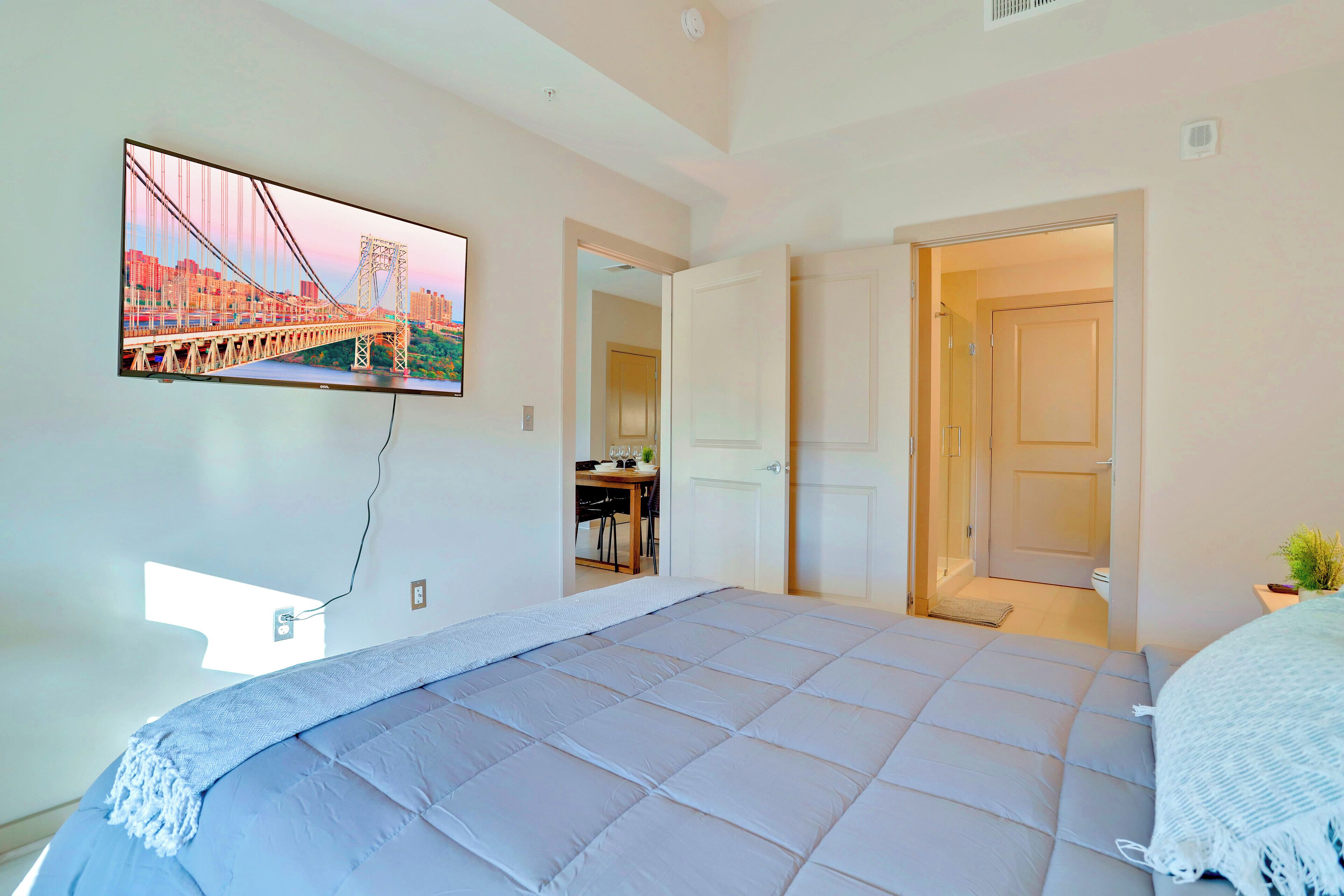 Une chambre avec un grand lit, un téléviseur fixé au mur et une porte donnant sur une autre pièce.
