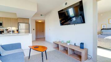 A modern living room with a sofa, a coffee table, a TV mounted on the wall, and a kitchen area in the background.