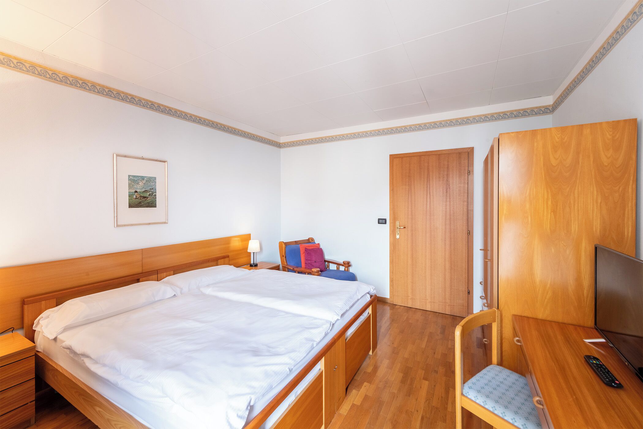 Une chambre à coucher avec un lit en bois, un bureau, une chaise, une télévision et une armoire.