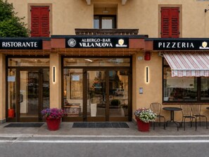 Un edificio con un cartel que indica 'Albergo-Bar Villa Nuova' y 'Pizzeria' en la planta baja.