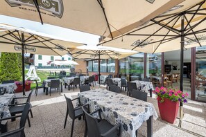 An outdoor patio with tables and chairs, umbrellas, and potted plants. - VILLA NUOVA (Romeno)