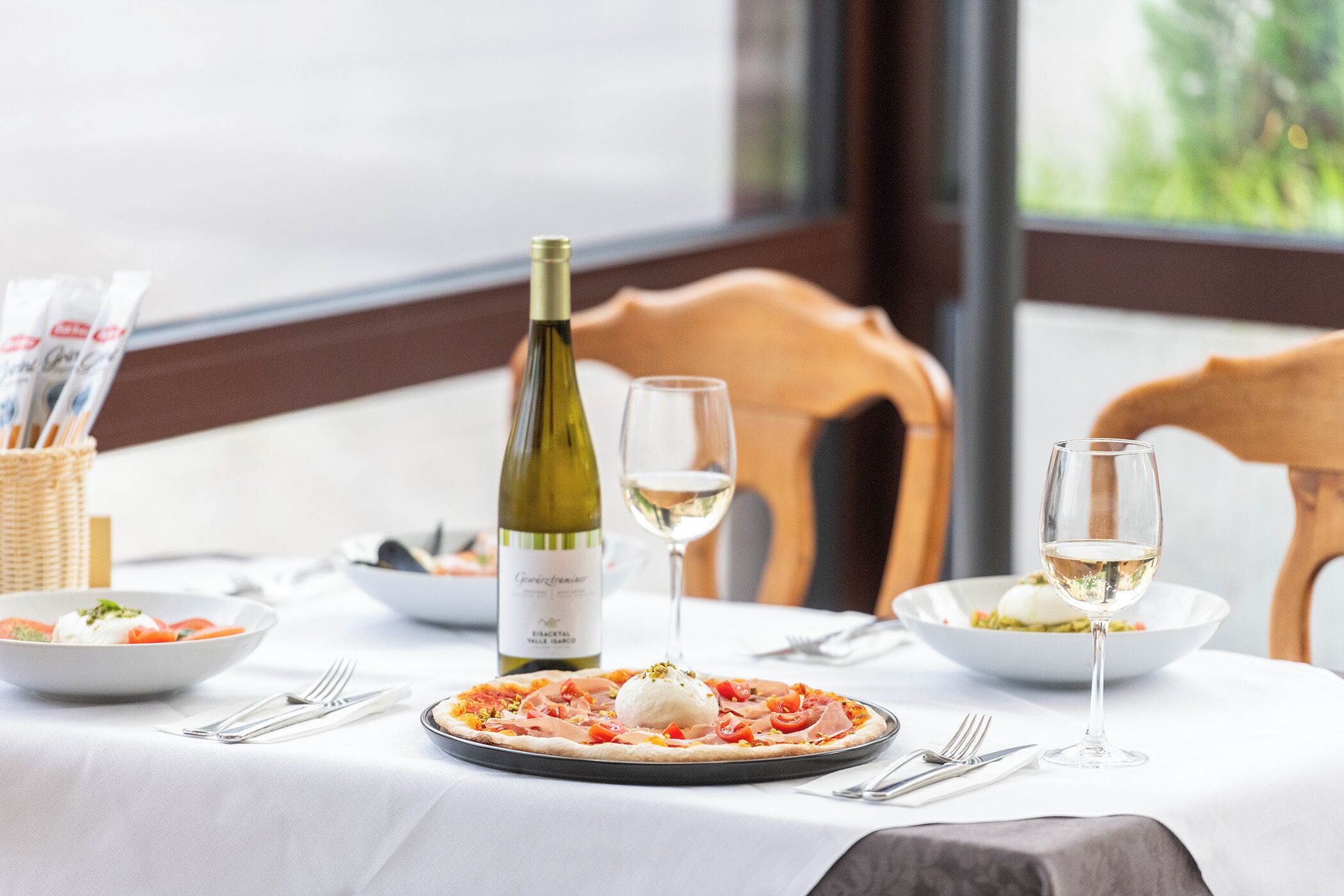 Una mesa de comedor con pizza, copas de vino y una botella de vino.