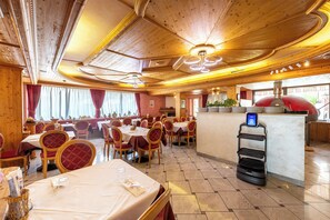 Un restaurante con techo y paredes de madera, mesas con sillas rojas y una barra de servicio con pantalla digital.