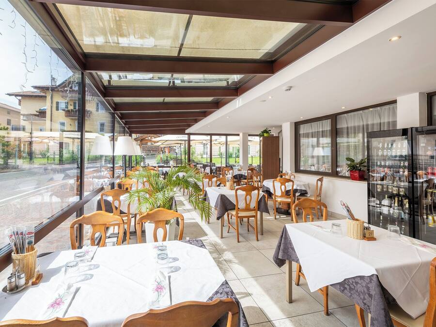 A restaurant with tables set for dining, a view of the street, and a refrigerator stocked with beverages.