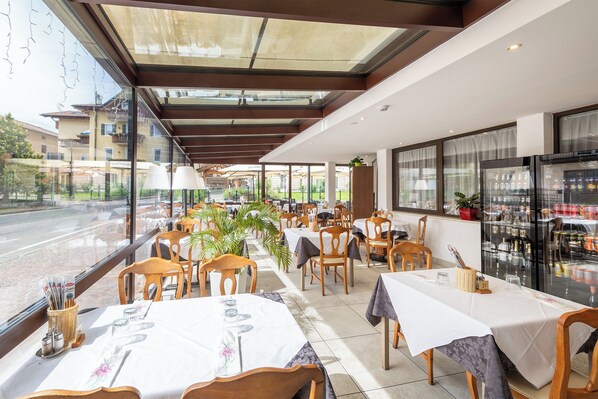 Un restaurante con mesas dispuestas para comer, vistas a la calle y un refrigerador lleno de bebidas.