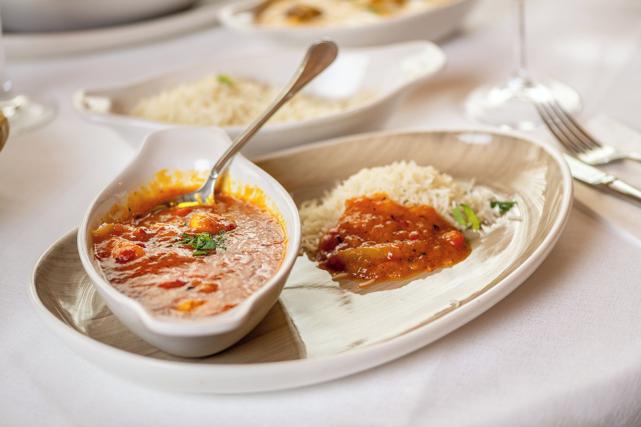 A plate with a bowl of soup and rice, a spoon, and a fork on a table.