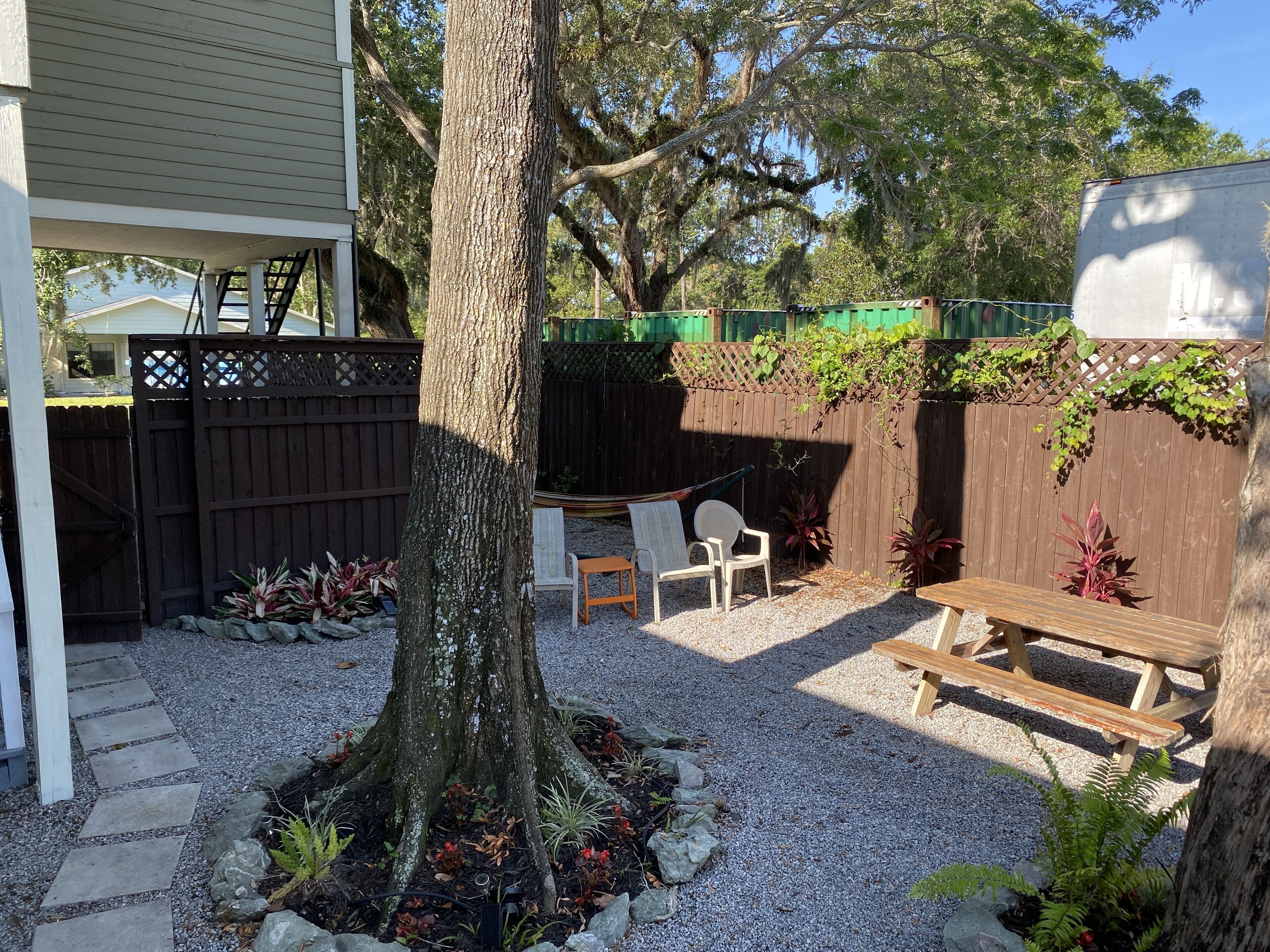 A backyard with a wooden deck, a tree, a bench, and a grill area.