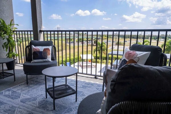 A balcony with a view of a highway and greenery. There are two chairs and a small round table. - Gorgeous 13BR Encore Resort Next to Disney - 348 (Kissimmee)