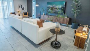 A modern living room with a white sofa, a coffee table, and a TV on the wall. - Gorgeous 13BR Encore Resort Next to Disney - 348 (Kissimmee)