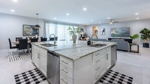 Una cocina moderna con una isla central, muebles blancos y un comedor con mesa y sillas.