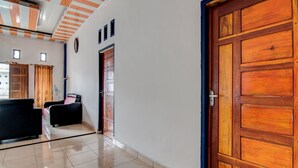Un couloir avec une porte en bois, un espace d’accueil avec un bureau et des chaises, et un sol carrelé.