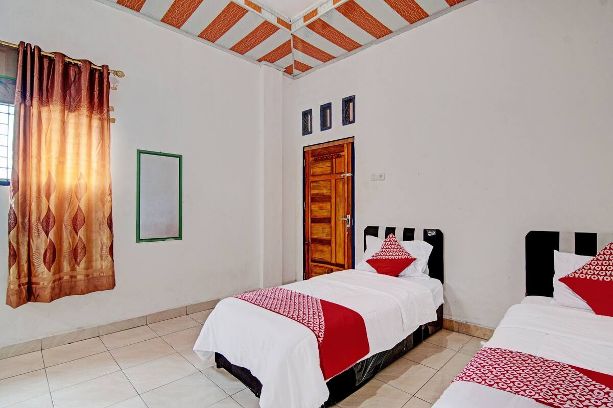 Une chambre avec deux lits, une porte en bois et un rideau à motifs.