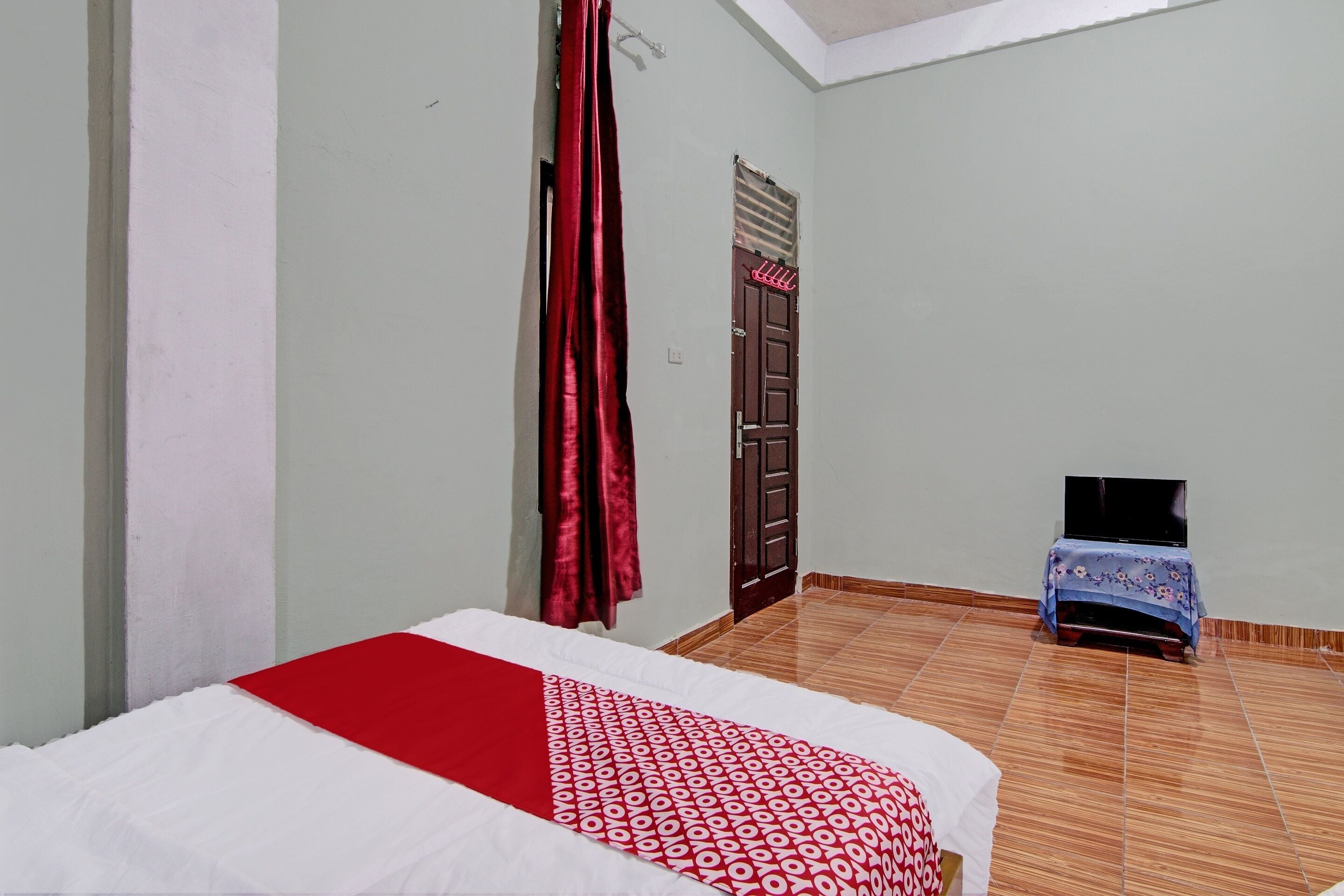 A bedroom with a bed, a door, a small table with a TV, and a window with curtains.