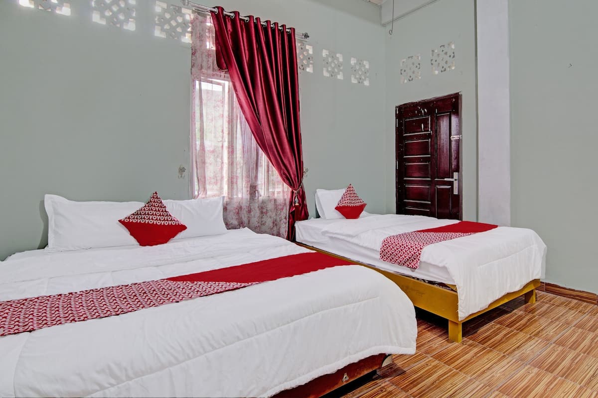 Une chambre d’hôtel avec deux lits, chacun agrémenté de draps blancs et de touches de couleur rouge, un plancher en bois et une porte ornée d’un panneau décoratif.