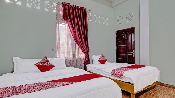 Une chambre d’hôtel avec deux lits, chacun agrémenté de draps blancs et de touches de couleur rouge, un plancher en bois et une porte ornée d’un panneau décoratif.