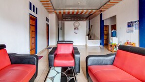 Un hall d’hôtel avec des canapés en cuir rouge et noir, un sol carrelé, un plafond à rayures orange et blanches et une horloge au mur.
