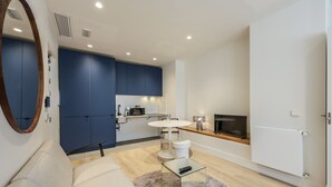 Una sala moderna con un sofá, una mesa de centro y un televisor. Cuenta con una zona de cocina con armarios azules y una mesa de comedor.