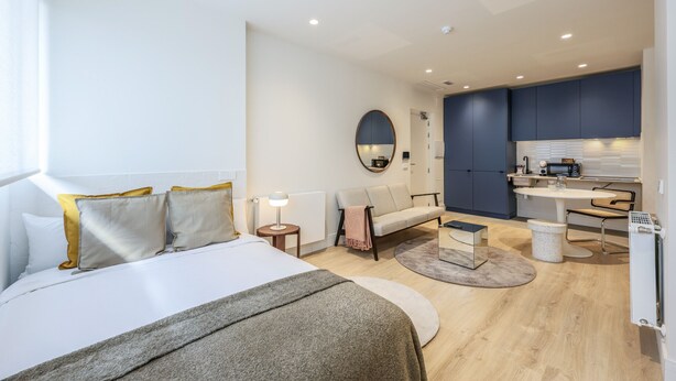 Una habitación de hotel moderna con cama, sofá, zona de comedor y kitchenette.