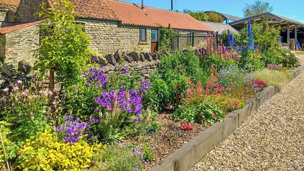 A stone building with a red-tiled roof, surrounded by a garden with various flowering plants. - 2 bedroom accommodation in Levisham, near Pickering (Levisham, near Pickering)