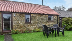 A stone building with a red-tiled roof, a small patio with a table and chairs, and a well-maintained lawn. - 2 bedroom accommodation in Levisham, near Pickering (Levisham, near Pickering)