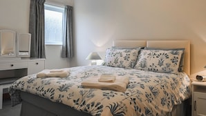 A neatly made bed with floral bedding, a bedside lamp, and a dresser with a mirror. - 2 bedroom accommodation in Levisham, near Pickering (Levisham, near Pickering)