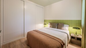 Ein Schlafzimmer mit einem Bett, Nachttischlampen und einem dunkelgrünen, kachelbeschlagenen Kopfteil.