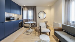 A modern kitchen with dark blue cabinets, a round dining table, a white chair, and a grey sofa.