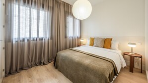 A neatly arranged bedroom with a large bed, a bedside table with a lamp, and a hanging light fixture.