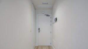 A narrow hallway with a white door at the end, a light switch on the wall, and a small air conditioning unit above the door.